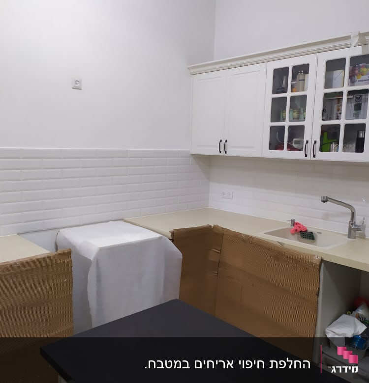 מטבח בשיפוץ עם ארונות מכוסים בנייר